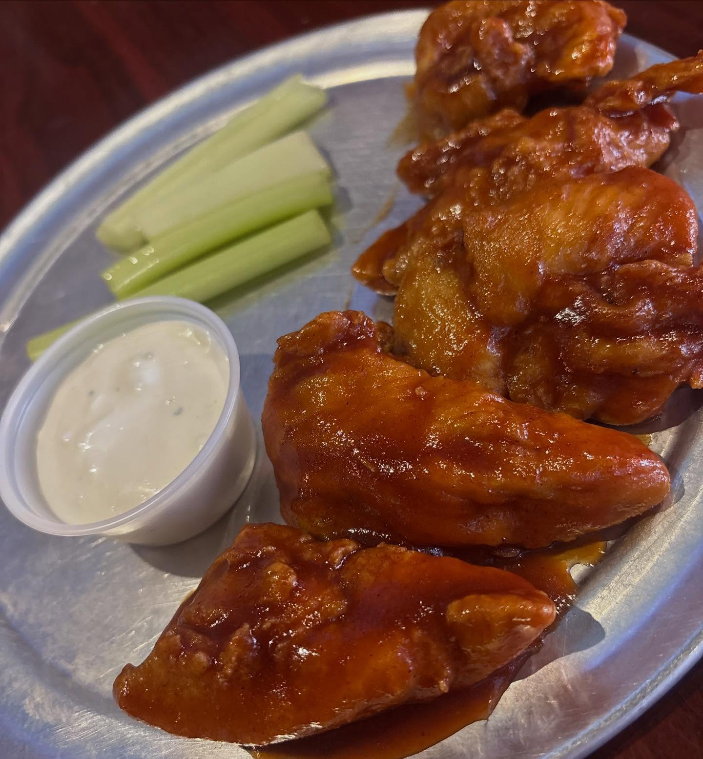 Chicken wings, celery sticks, and dipping sauce on a metal plate.