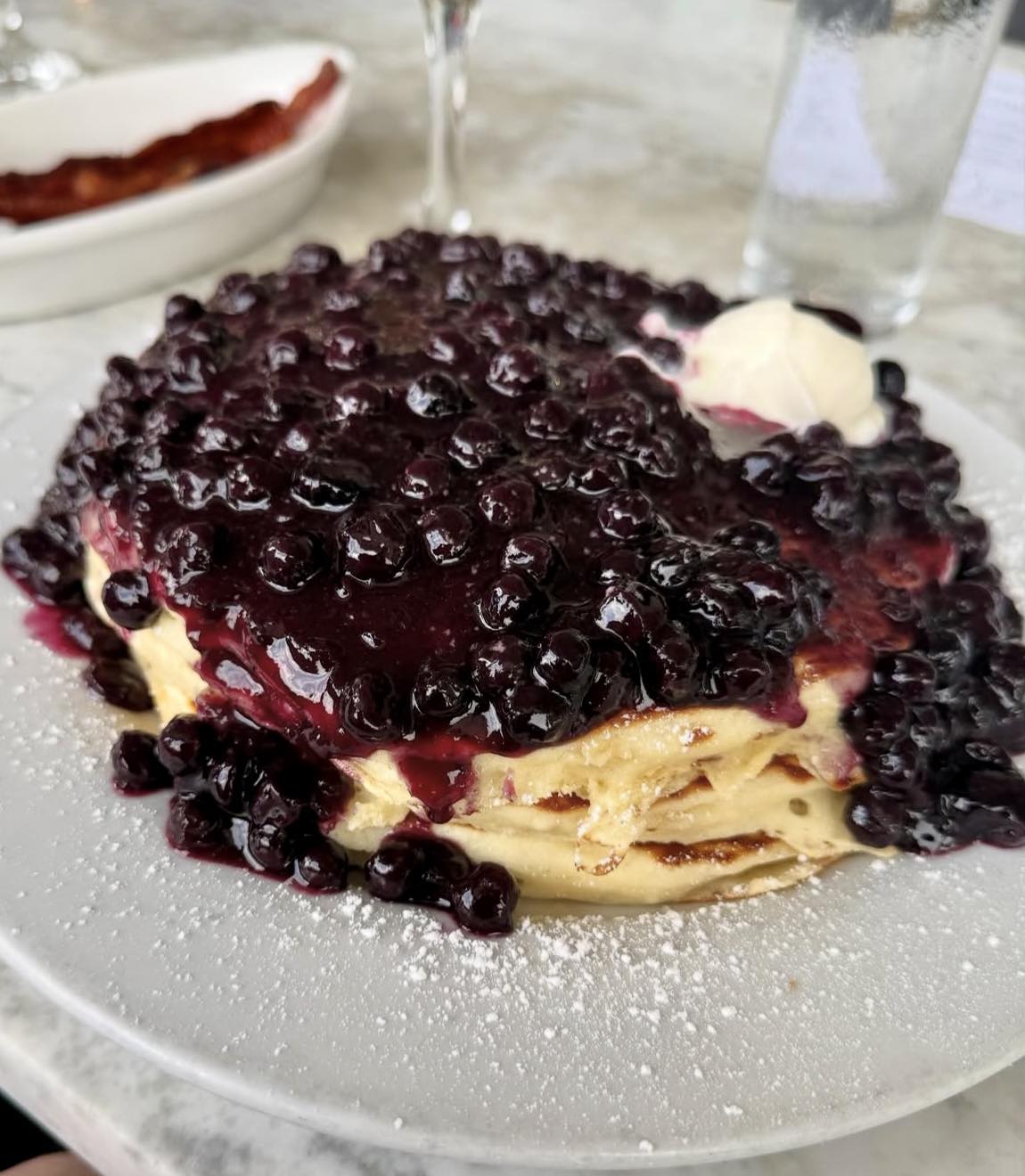Stack of pancakes covered in blueberry topping, cream, and powdered sugar.