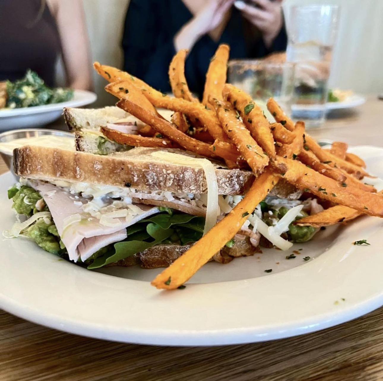 Sandwich with turkey, avocado, greens, and a side of sweet potato fries.