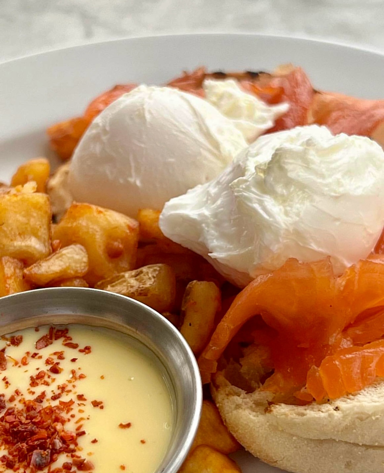 Poached eggs, smoked salmon, fried potatoes, and sauce with red flakes.