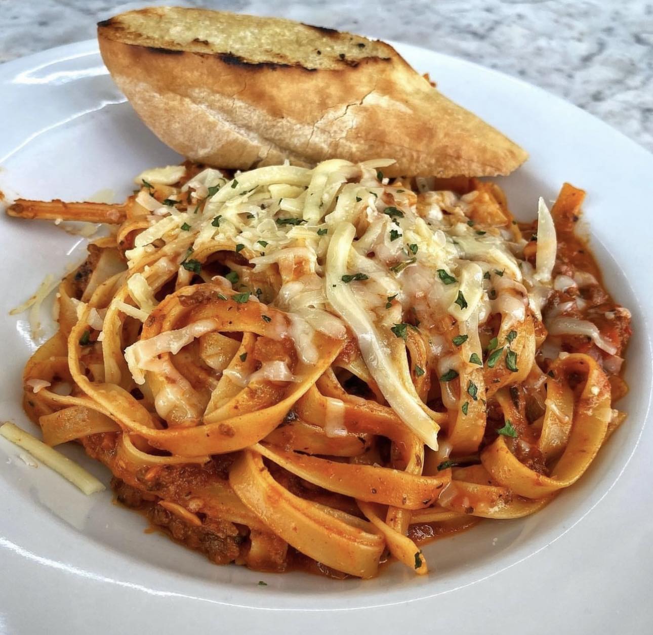 Pasta with red sauce, melted cheese, green herbs, and toasted bread.