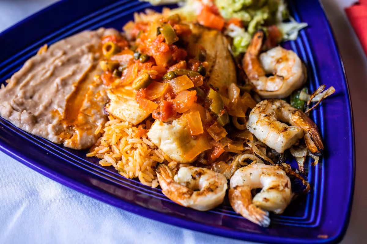 Refried beans, rice, grilled shrimp, and sauced entree on blue plate.