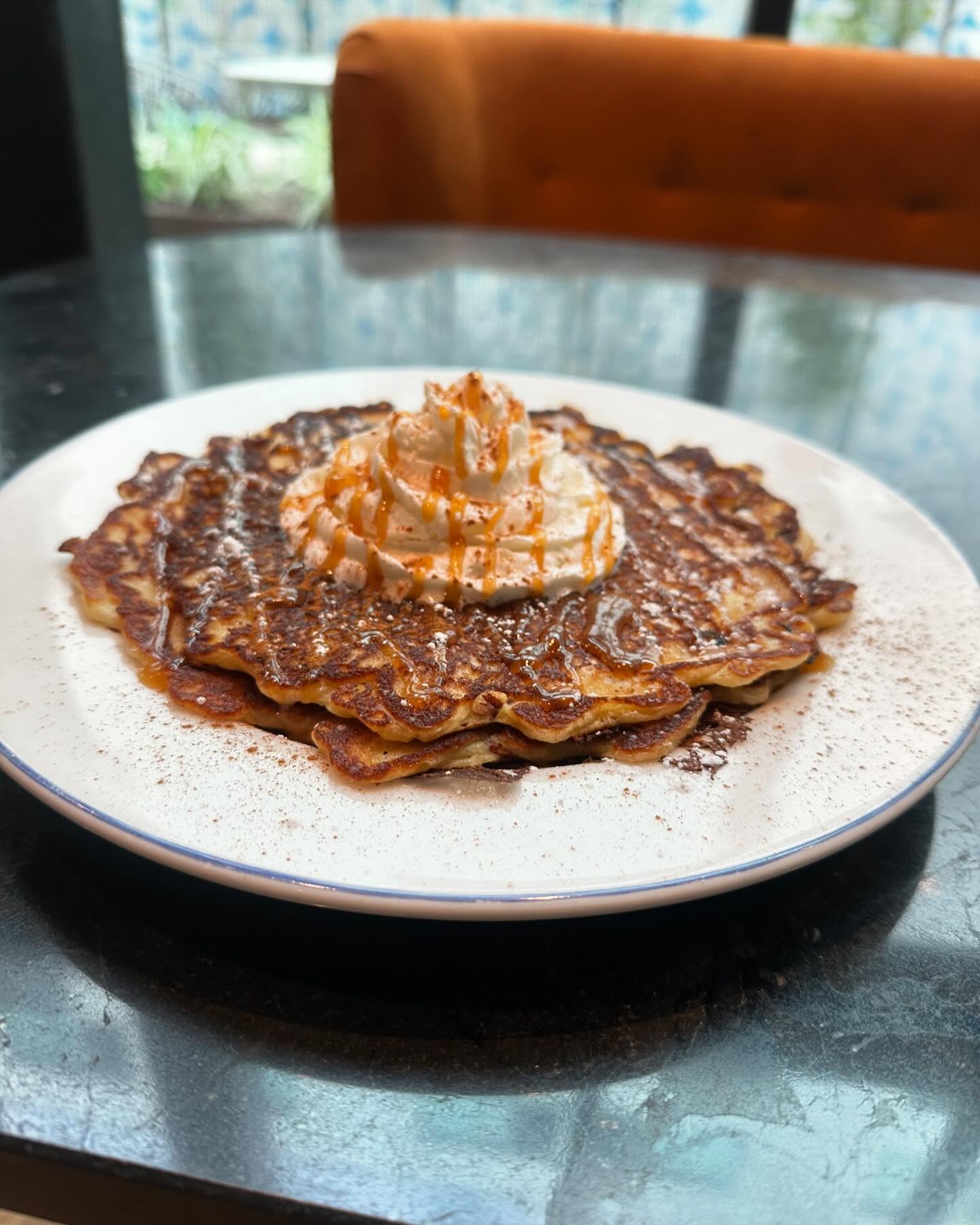 Pancakes topped with whipped cream and caramel drizzle on a plate.