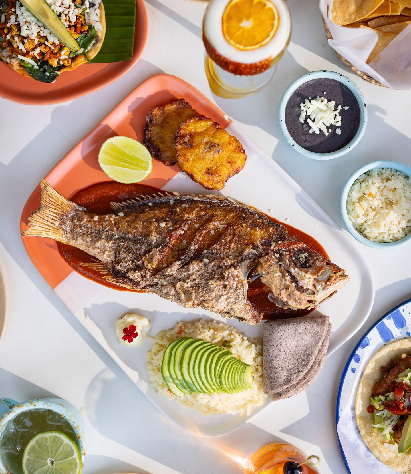 Whole fried fish, plantains, rice, black beans, and drinks.