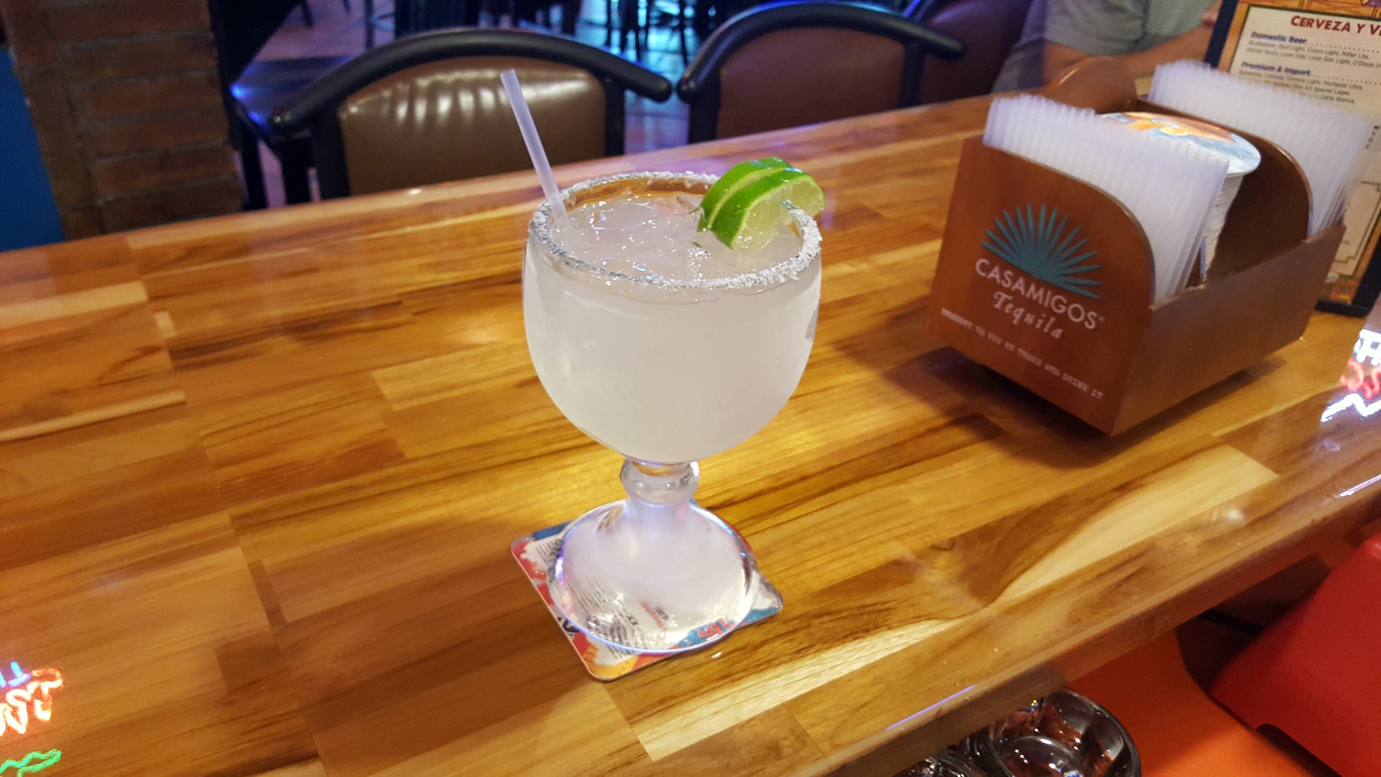 Margarita cocktail with ice, lime, and a salted rim on a bar.