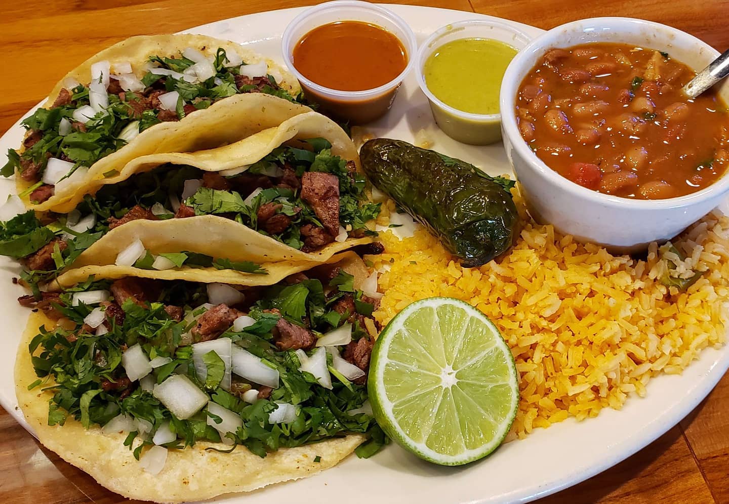 Three tacos, rice, beans, jalapeño, lime, and two salsas.