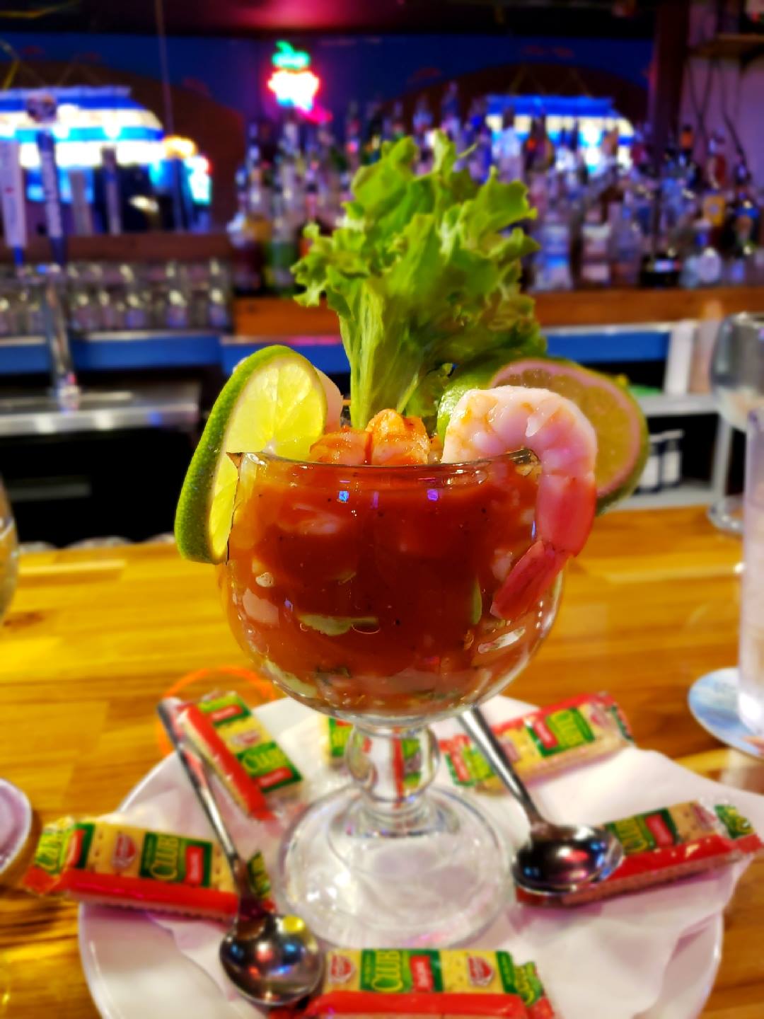 Glass of shrimp cocktail with lime, lettuce, and crackers at a bar.