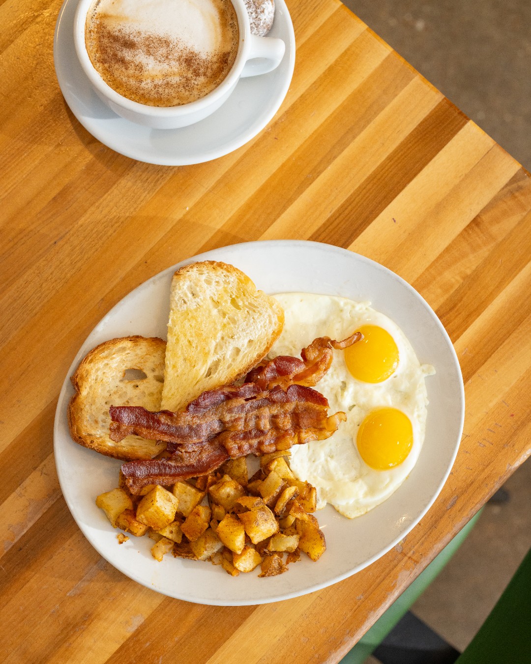 Breakfast plate with fried eggs, bacon, toast, home fries, and coffee.