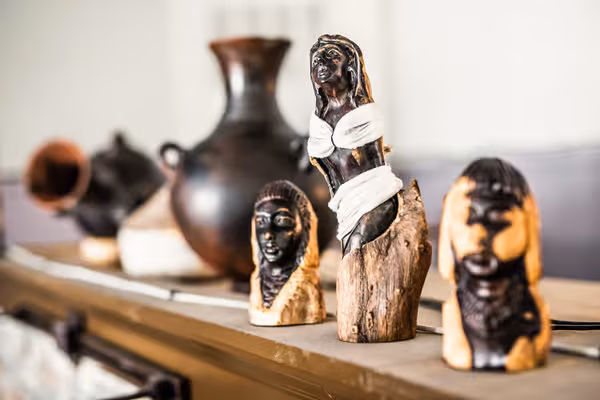 Three carved wooden figures and dark pottery on a shelf.