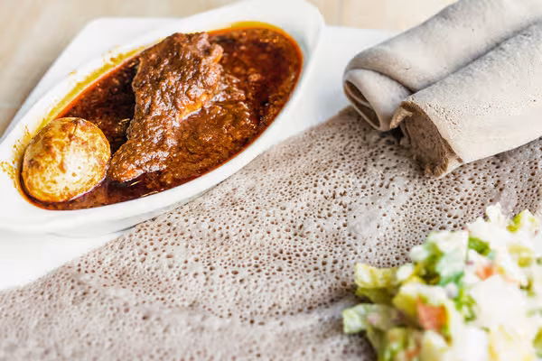 Ethiopian Doro Wat with injera bread, hard-boiled egg, and salad.