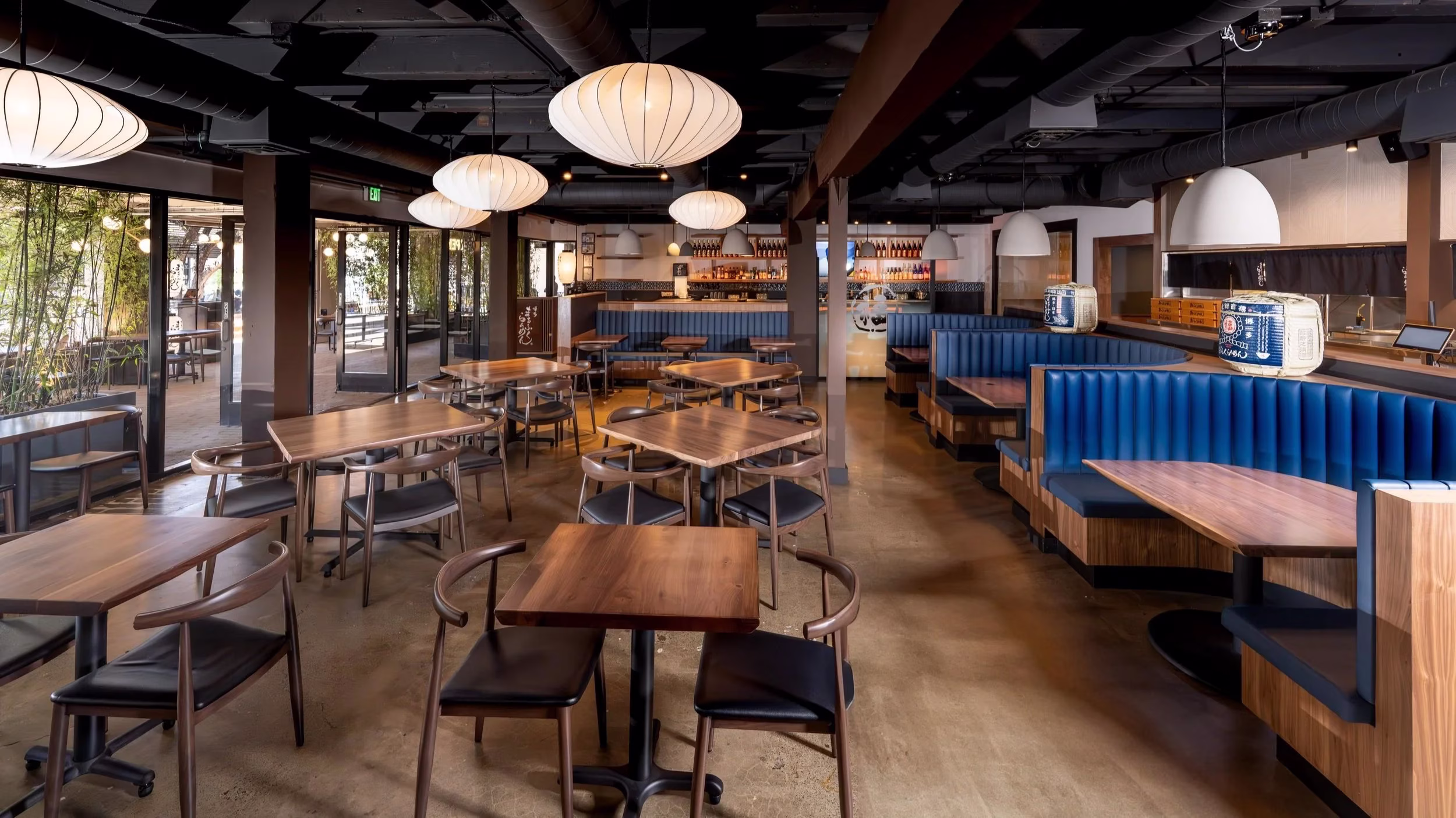 Restaurant interior with wooden tables, blue booths, and white globe lanterns.