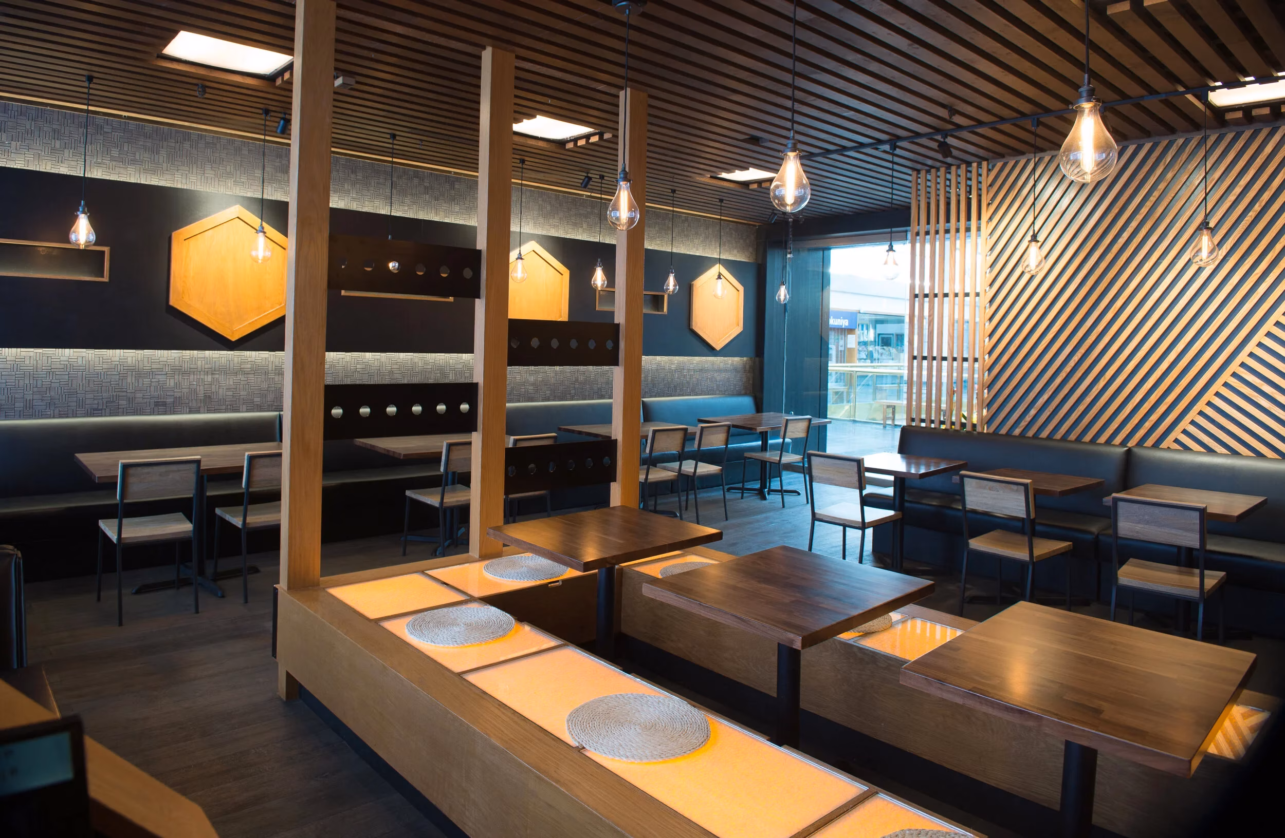 Modern restaurant interior with wood panels, black booths, and illuminated counters.