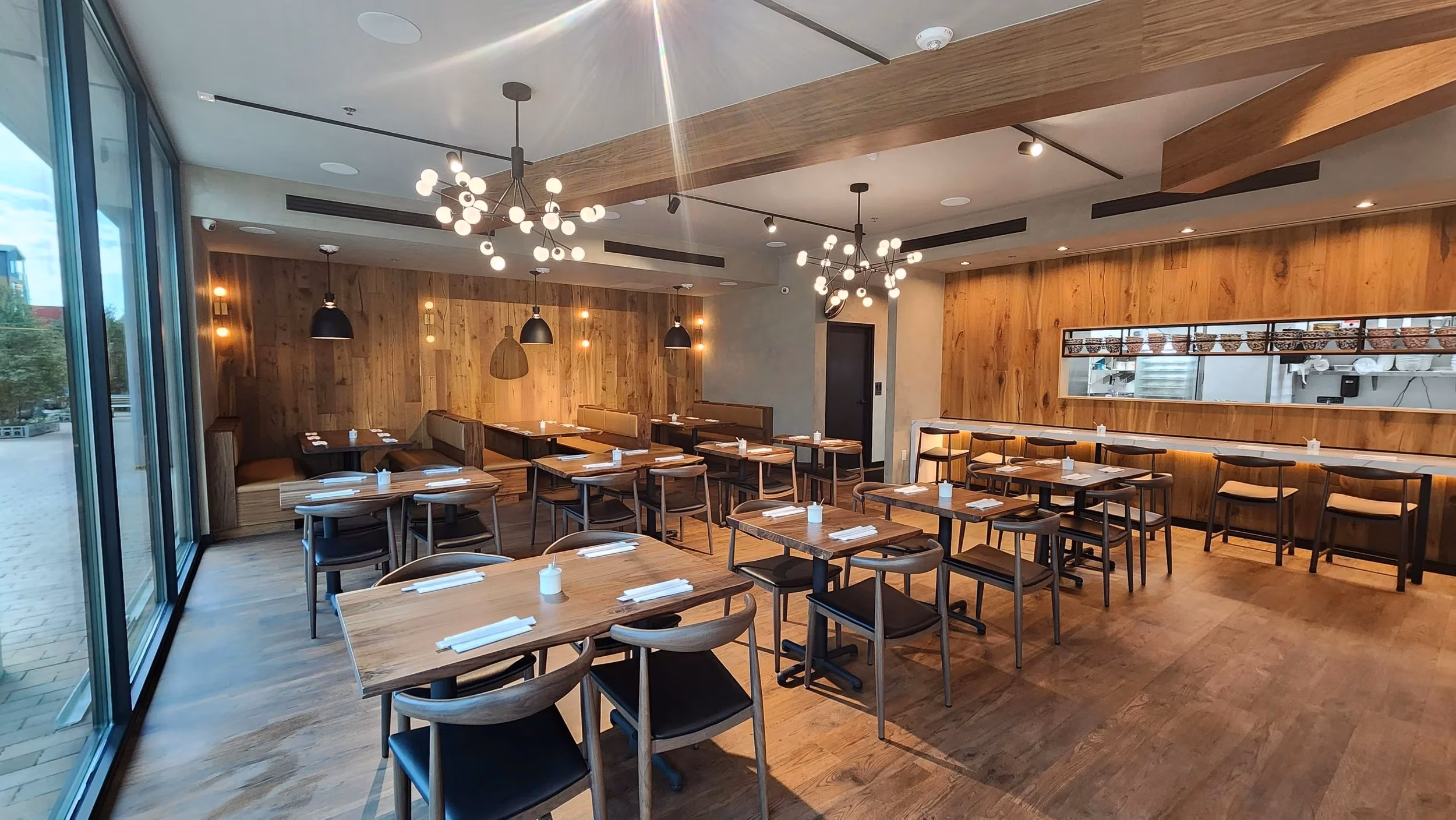 Modern restaurant with wooden tables, chairs, wood walls, and open kitchen.