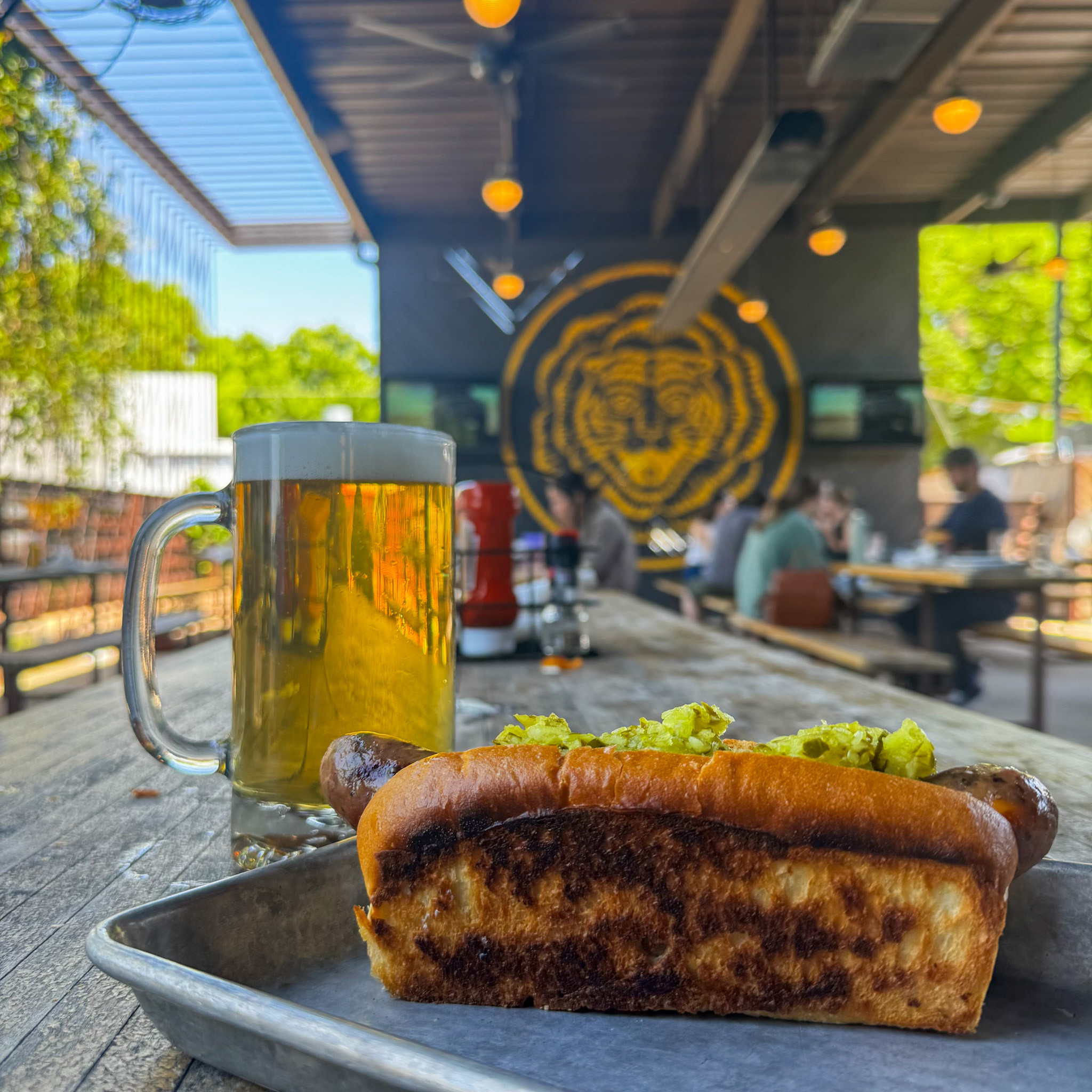 Grilled hot dog with relish and beer on a wooden table.