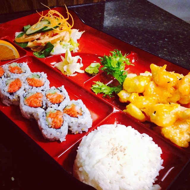 Japanese bento box with sushi, rice, salad, and sauced shrimp.