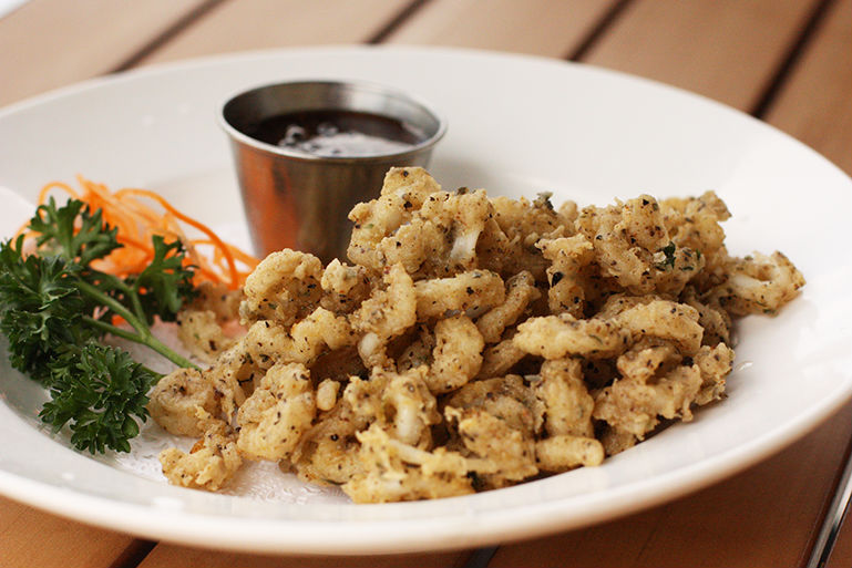 A plate of fried calamari with dipping sauce, parsley, and carrots.