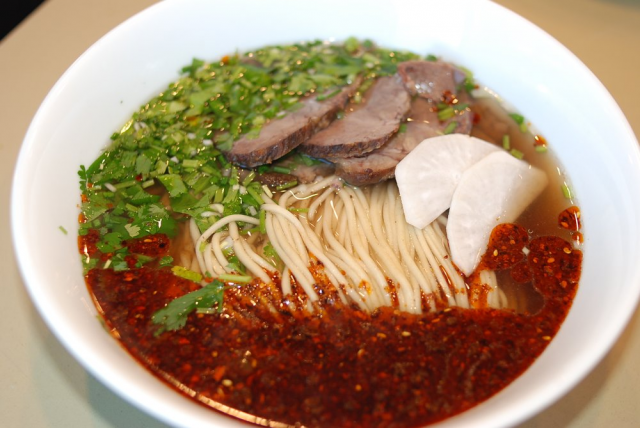 Bowl of beef noodle soup with cilantro, radish, and chili oil.