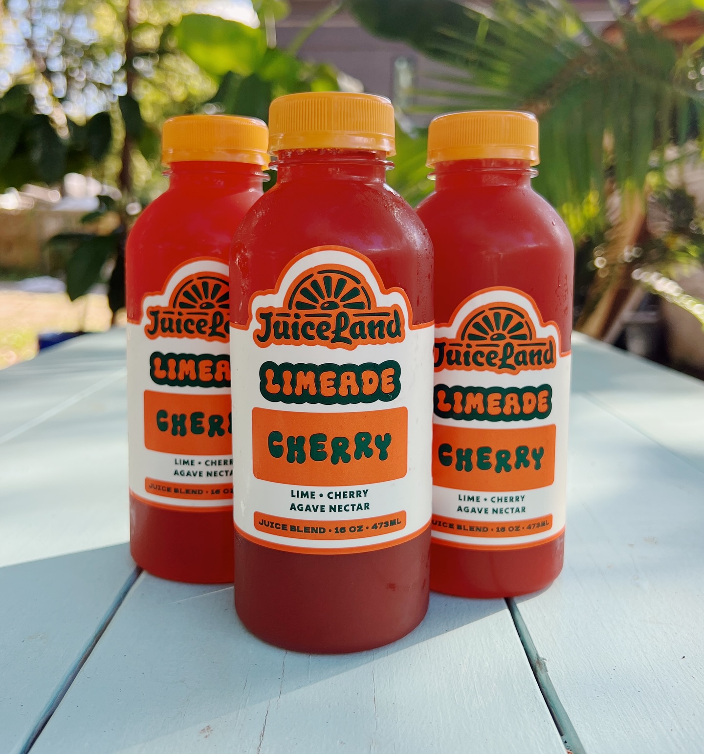 Three red bottles of JuiceLand Limerade Cherry juice blend outdoors.