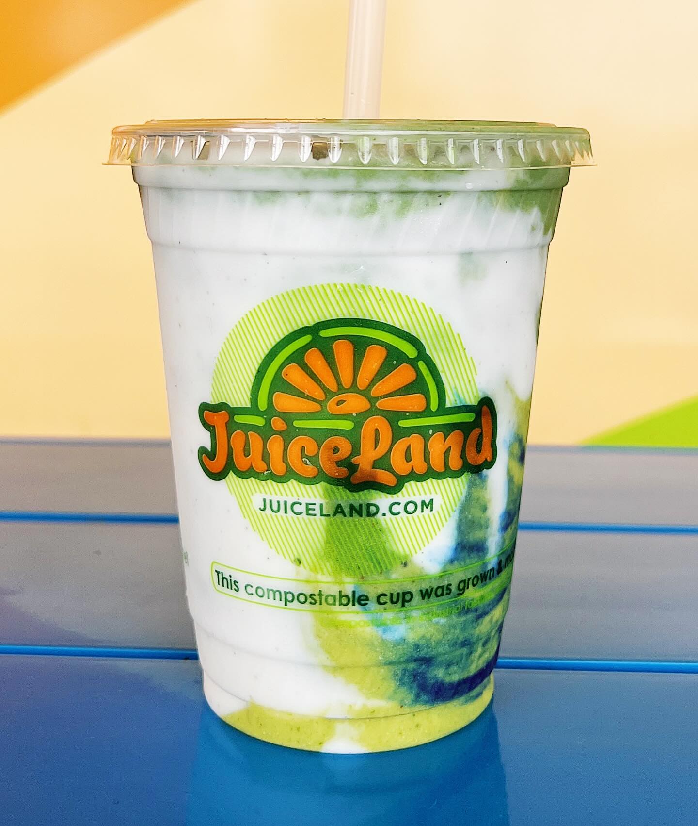 JuiceLand cup with layered white, green, and blue smoothie and straw.