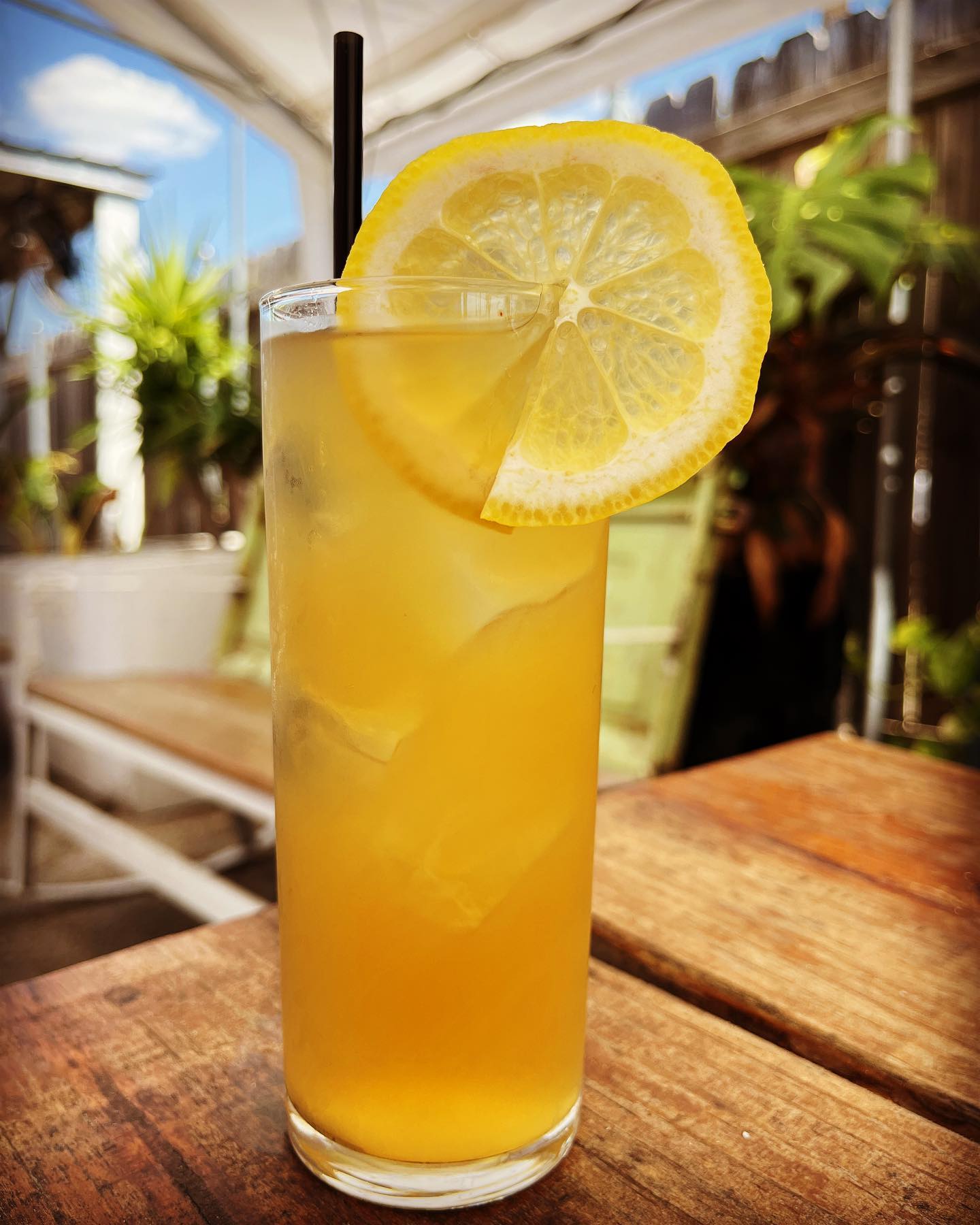 Tall glass of iced lemon drink on a wooden table outdoors.
