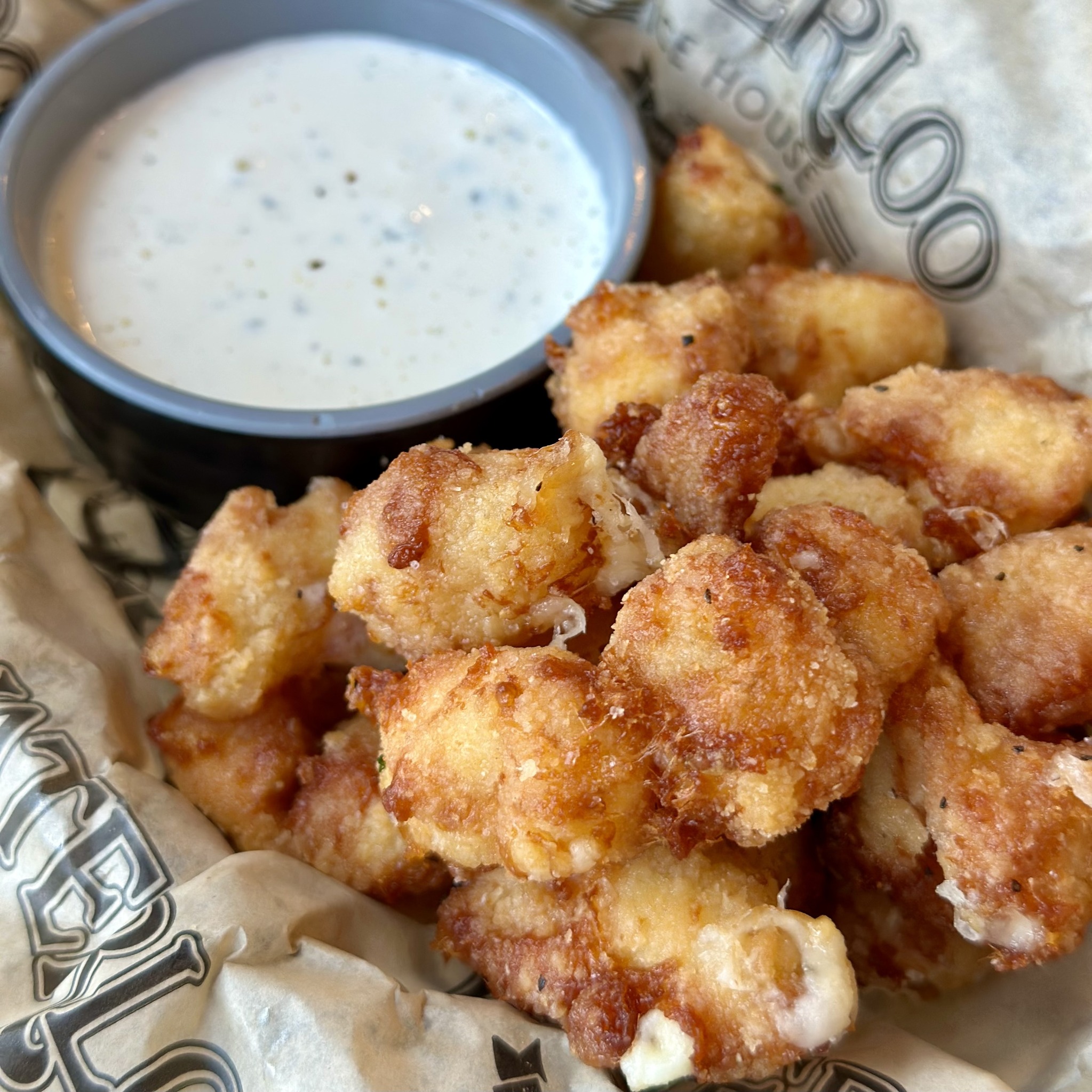 Golden fried cheese curds served with a side of white dipping sauce.