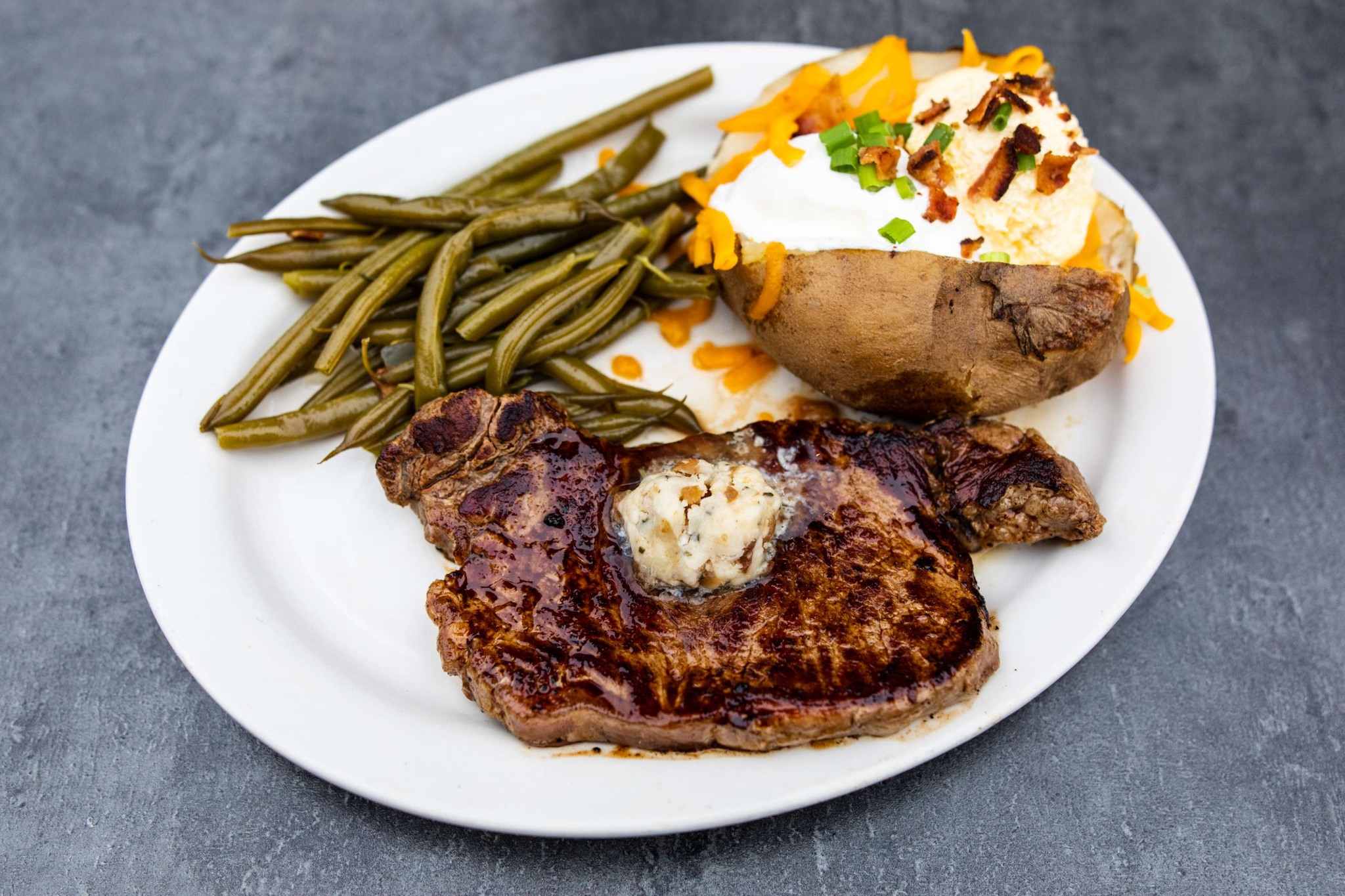 Plate with steak, loaded baked potato, and green beans.