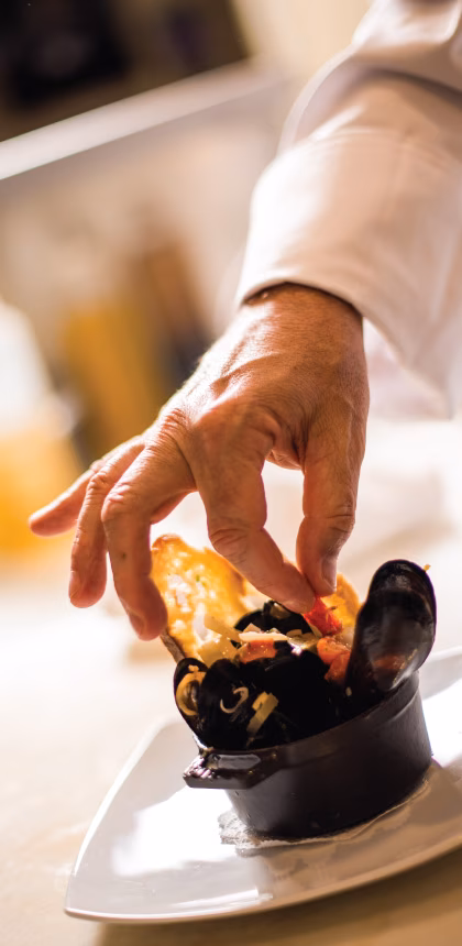 Close-up: Chef's hand adding red ingredient to a mussel dish.
