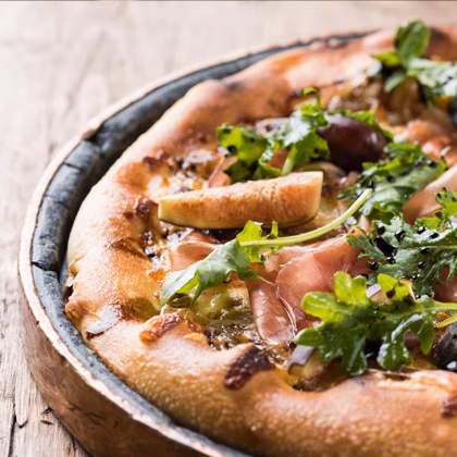Gourmet pizza with figs, prosciutto, arugula, and balsamic glaze in a skillet.