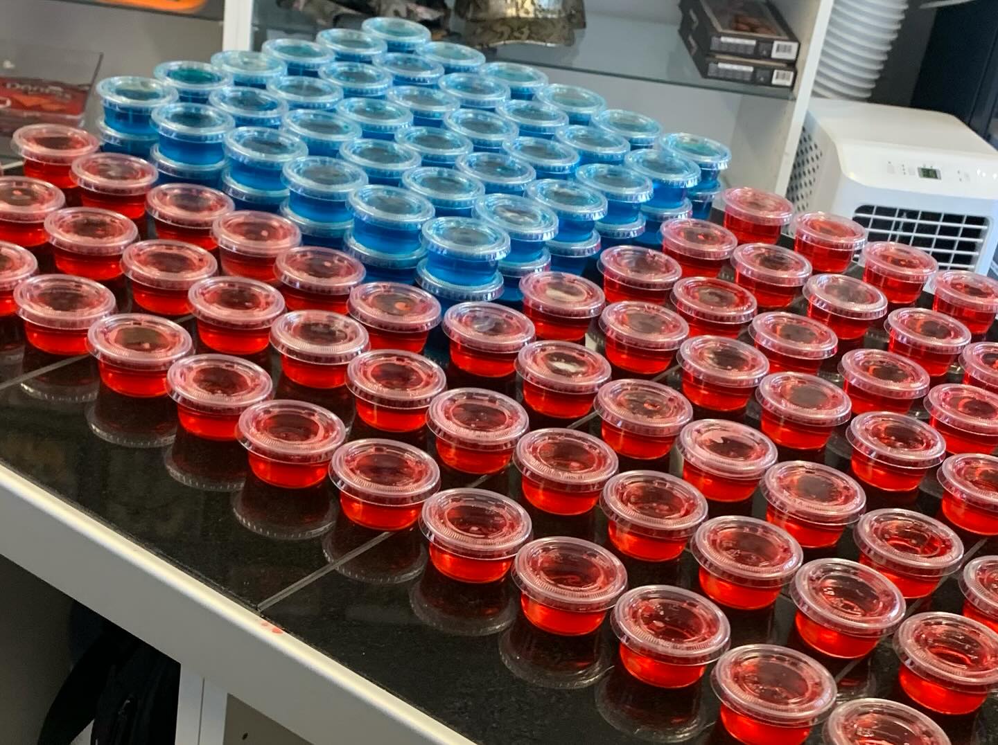 Numerous plastic cups of red and blue gelatin on a counter.