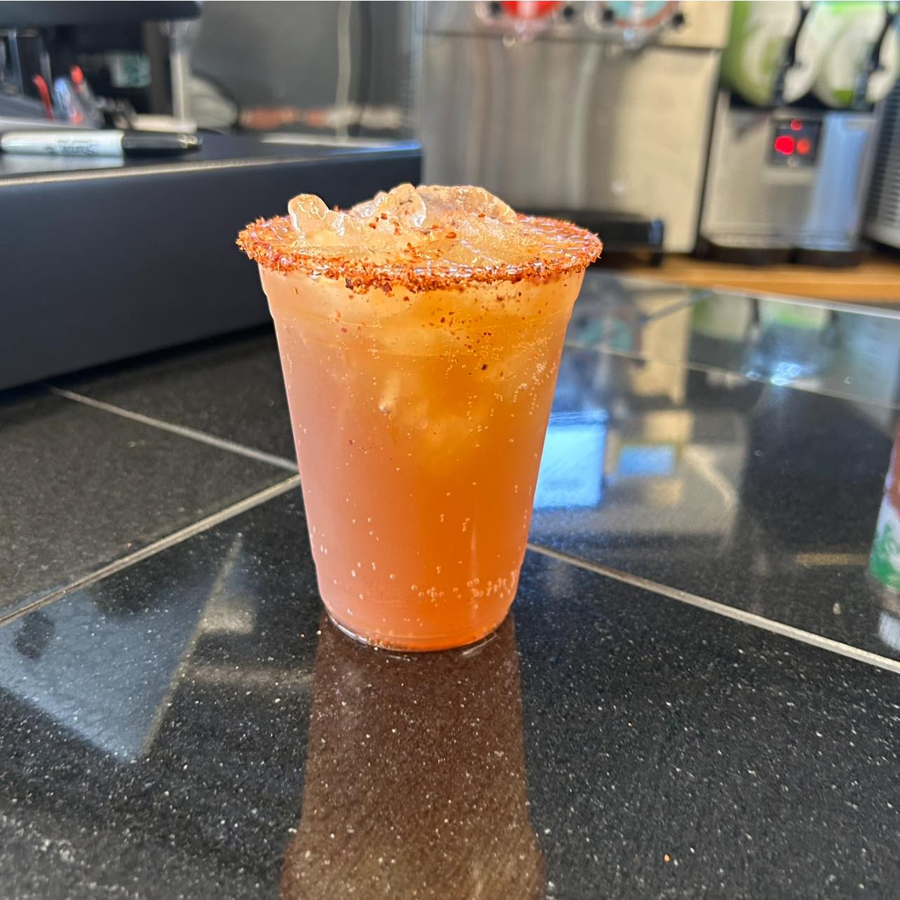 Orange iced drink with a spiced rim on a dark counter.