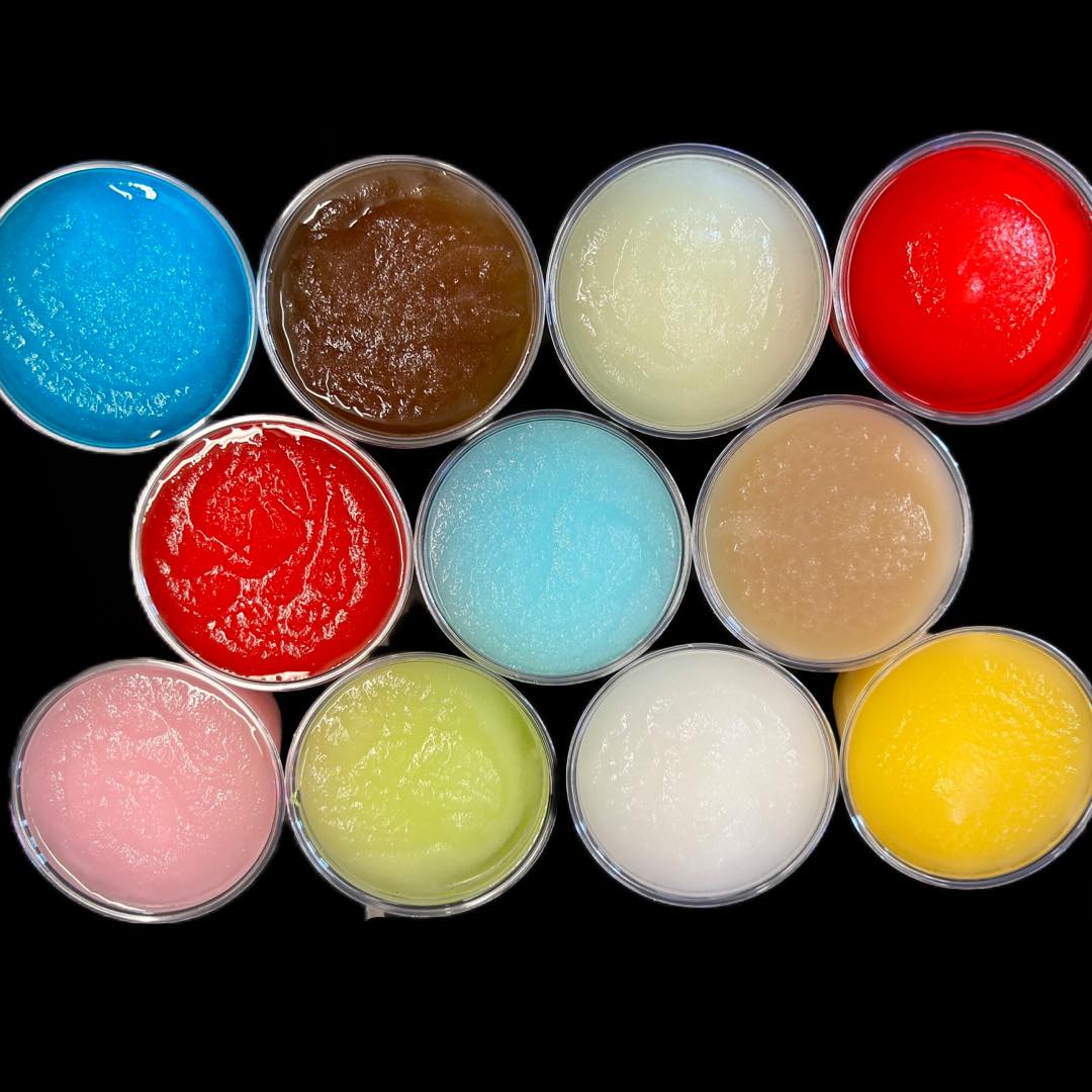 Twelve cups filled with various brightly colored frozen slush drinks.