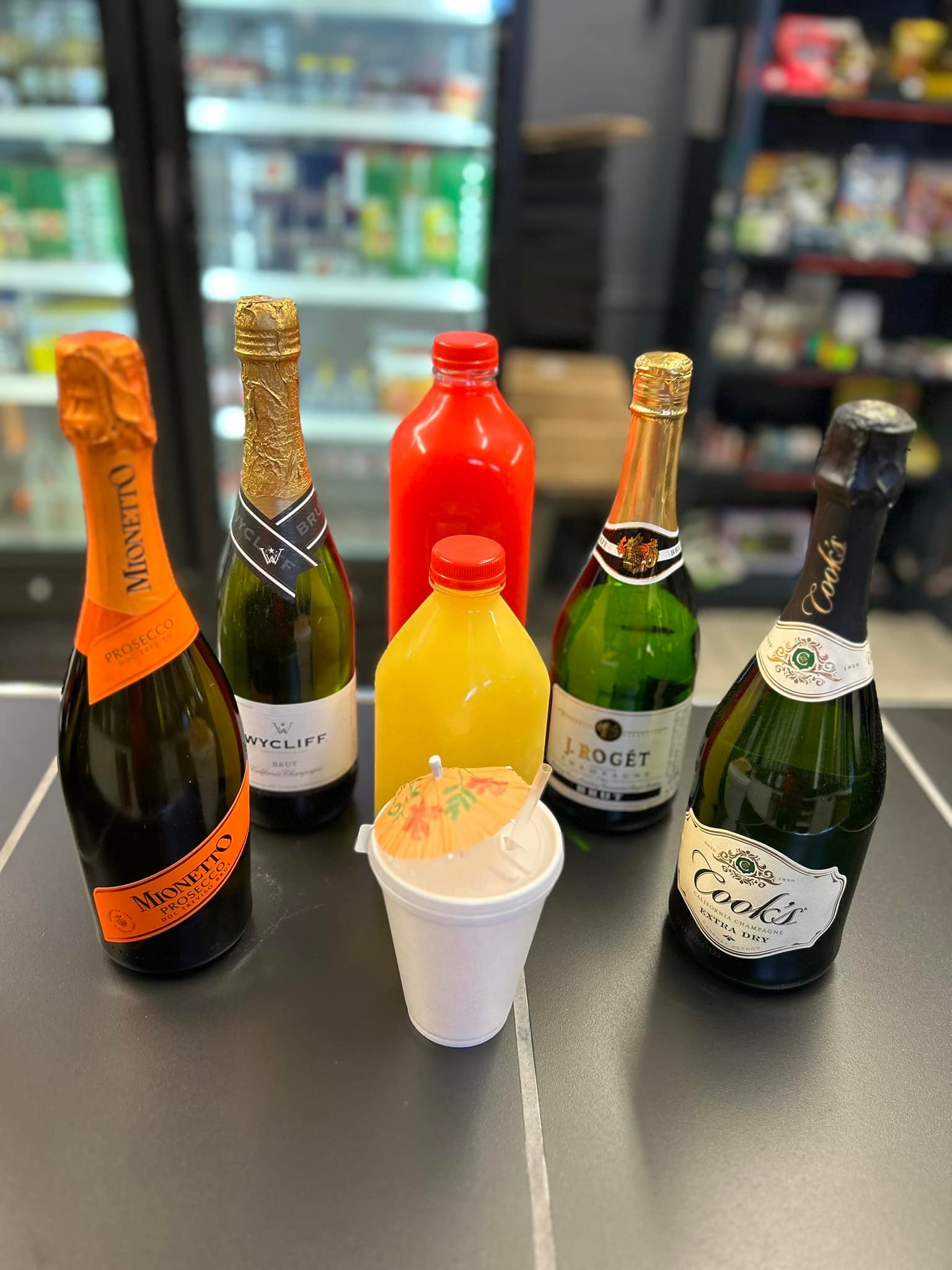 Bottles of champagne, prosecco, and juice with a festive cup.