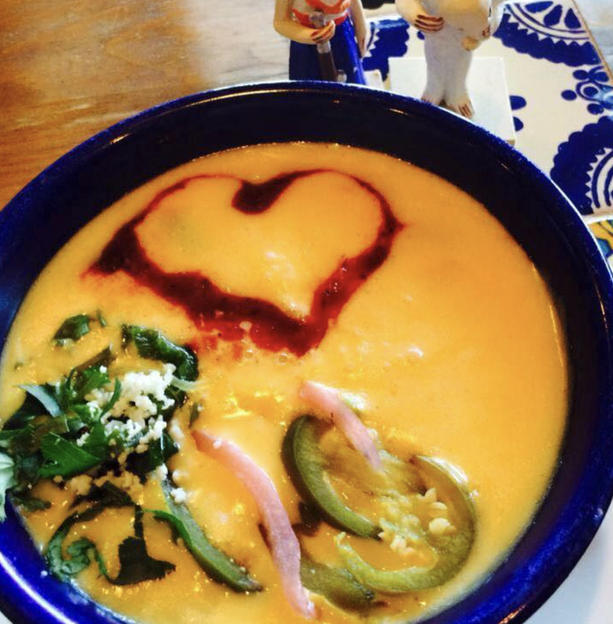 Creamy yellow dish with heart-shaped sauce, peppers, herbs, and cheese.