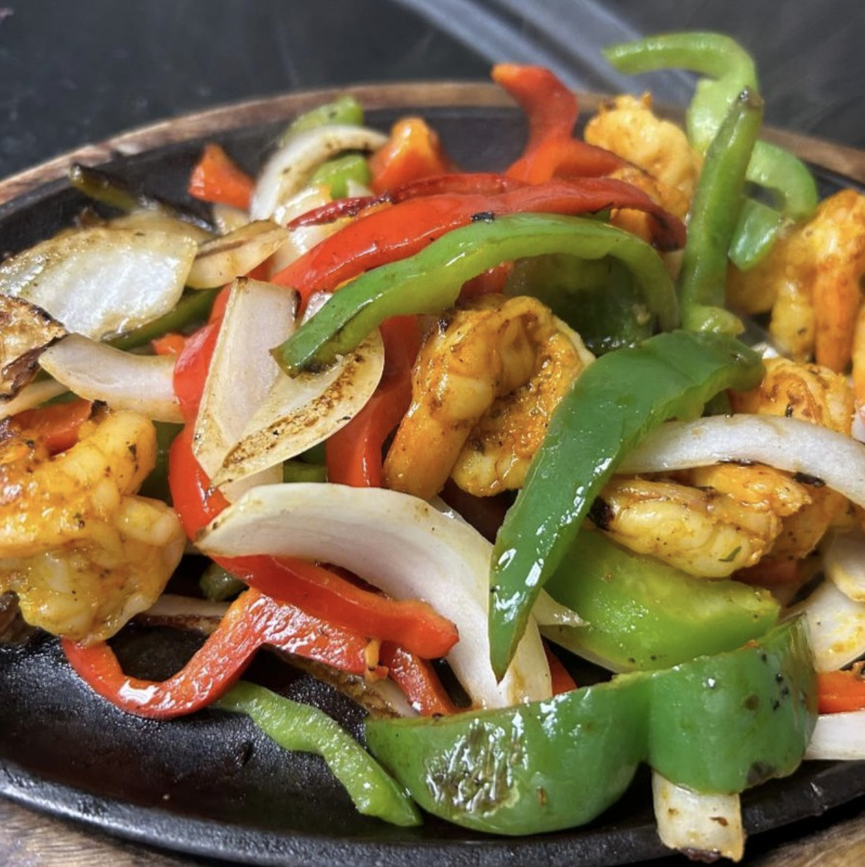 Shrimp, peppers, and onions cooked on a hot skillet.