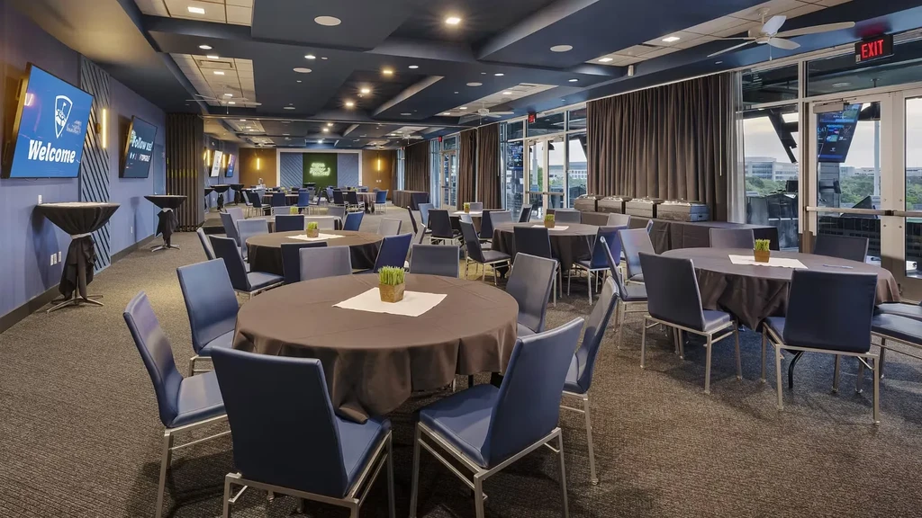 Modern blue event hall with tables, chairs, windows, and display screens.