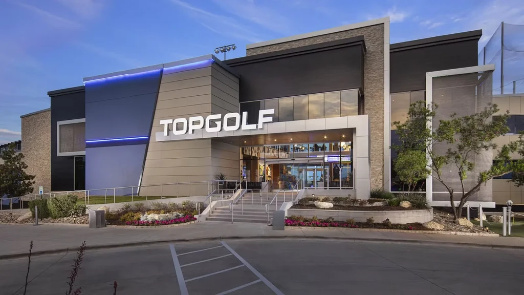 Exterior view of a modern Topgolf building with a visible golf net.