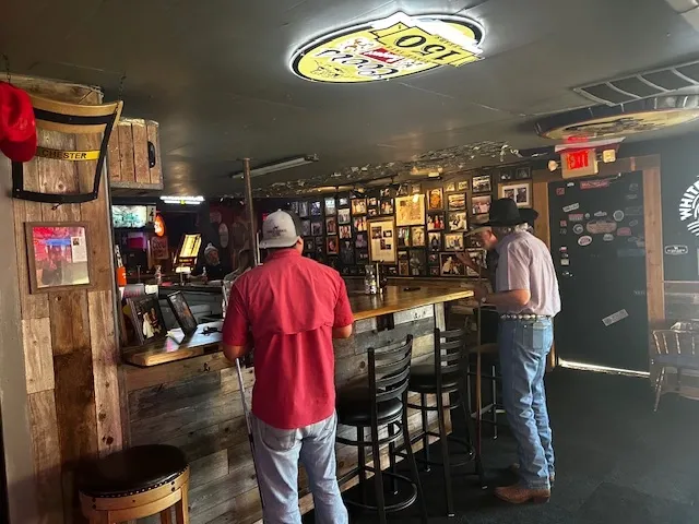 Two men standing at a wooden bar inside a dimly lit bar.
