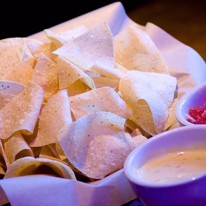 Basket of tortilla chips with small bowls of cheese dip and salsa.