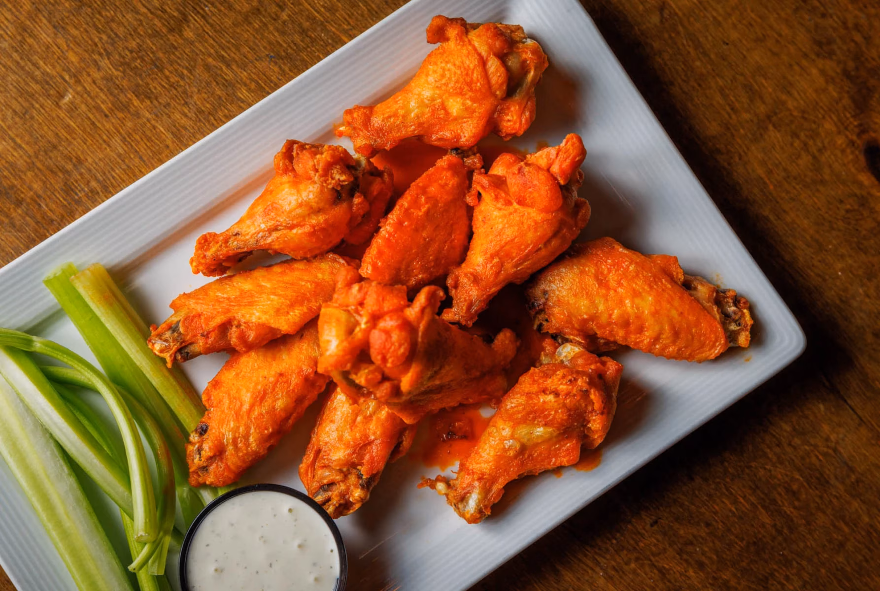 Buffalo wings, celery sticks, and white dipping sauce on a plate.