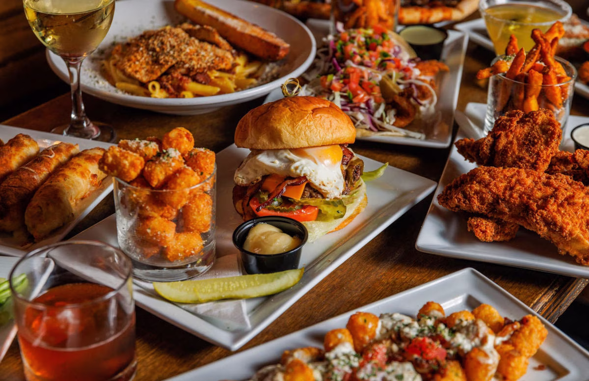 Table full of burgers, fried chicken, pasta, tater tots, and drinks.