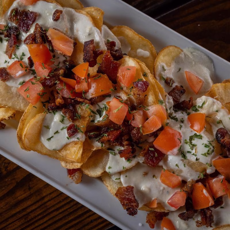 Potato chips topped with creamy sauce, diced tomatoes, and bacon.
