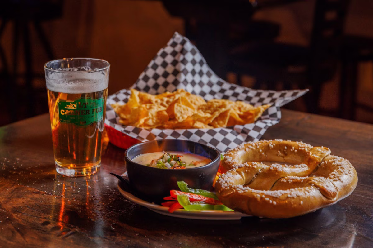Beer, salted pretzel, cheese dip, chips, and bell peppers.