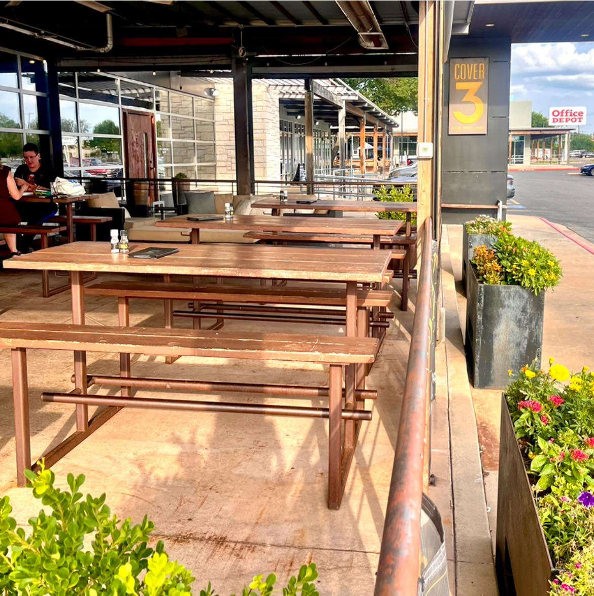 Outdoor patio with wooden picnic tables at Cover 3 restaurant.