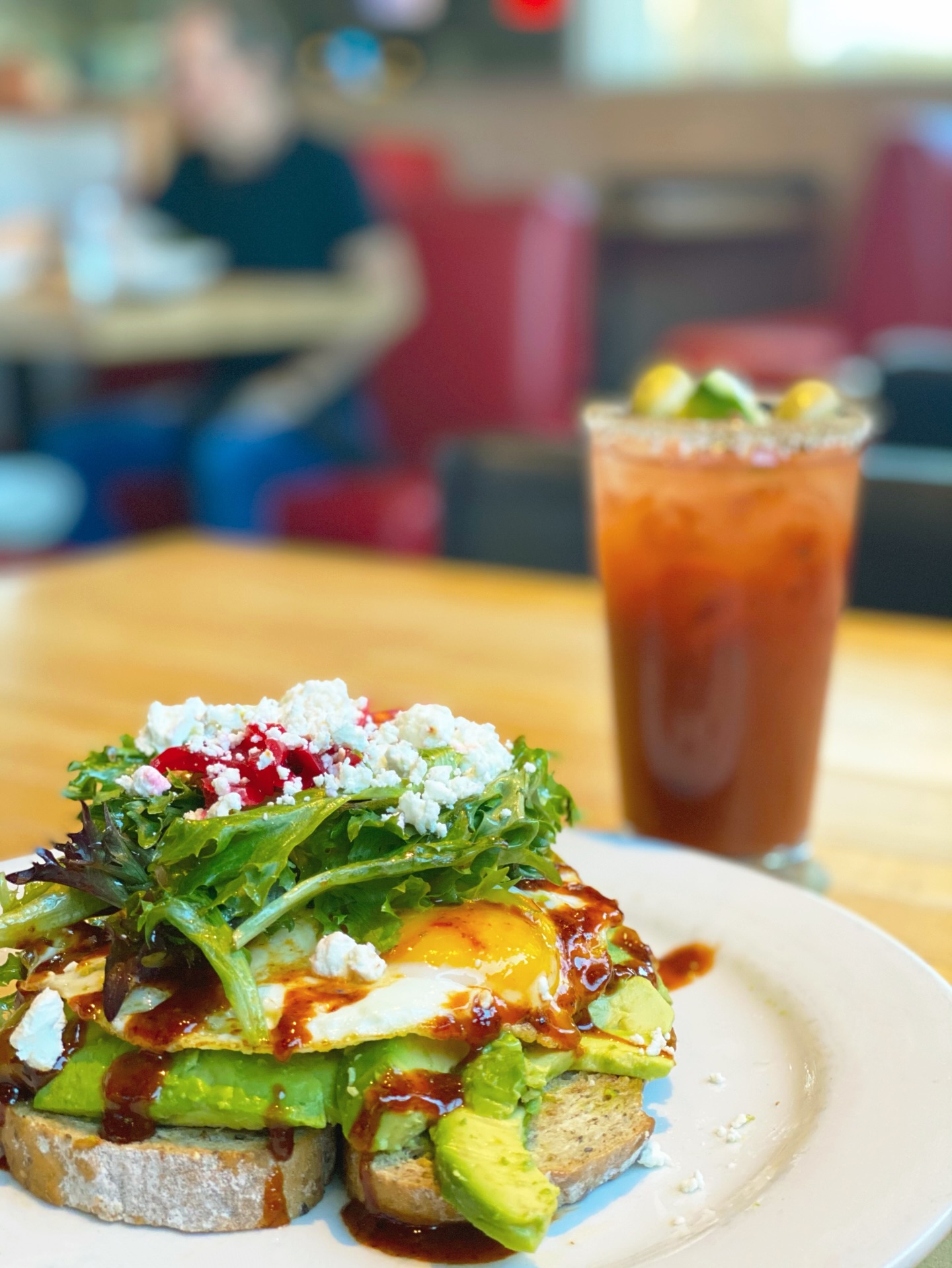 Avocado toast with fried egg and salad, and a drink in a restaurant.