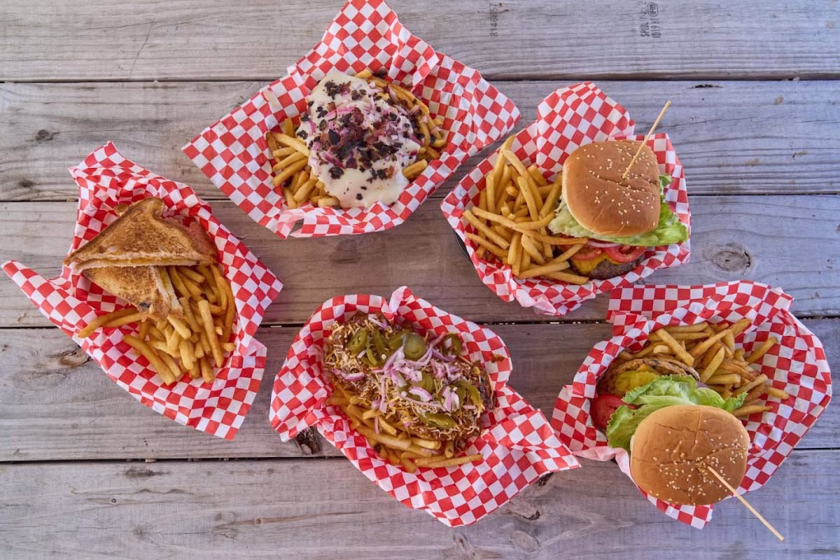 Five fast-food baskets of burgers, fries, and a sandwich on wood.