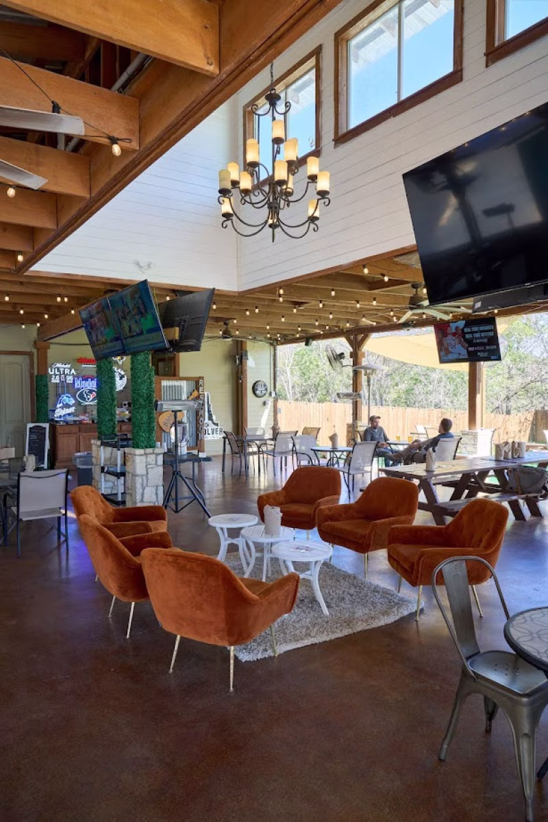 Spacious indoor-outdoor bar with orange chairs, wooden beams, and TVs.