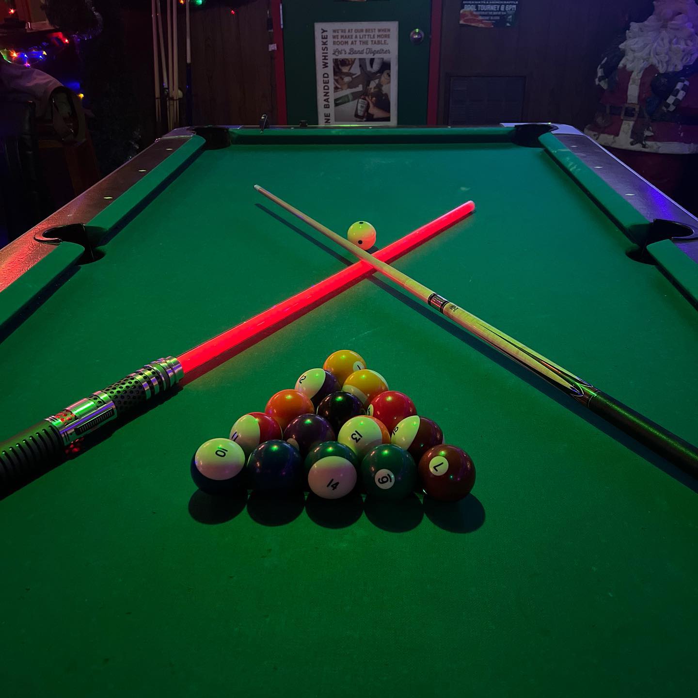 Pool table with racked balls, cue, and red lightsaber prop.