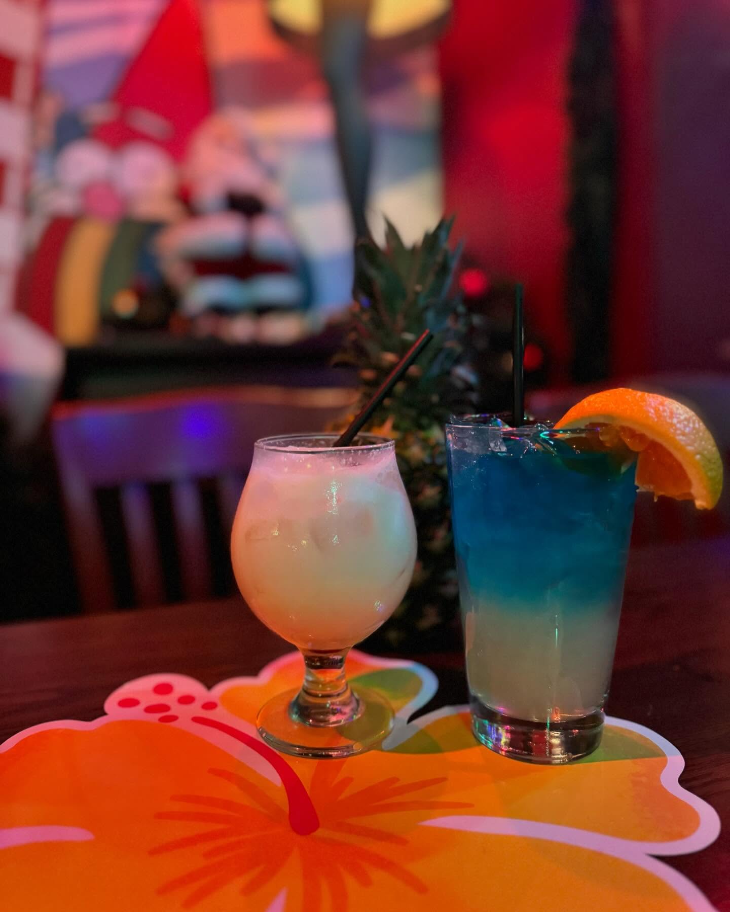 A creamy white and a layered blue cocktail on hibiscus coasters.