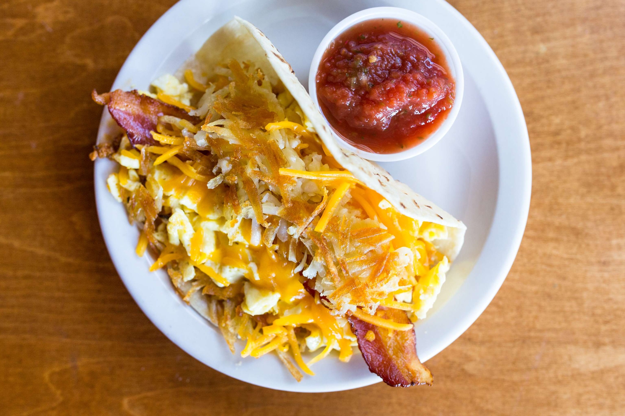 Breakfast taco with bacon, eggs, cheese, hash browns, and salsa.