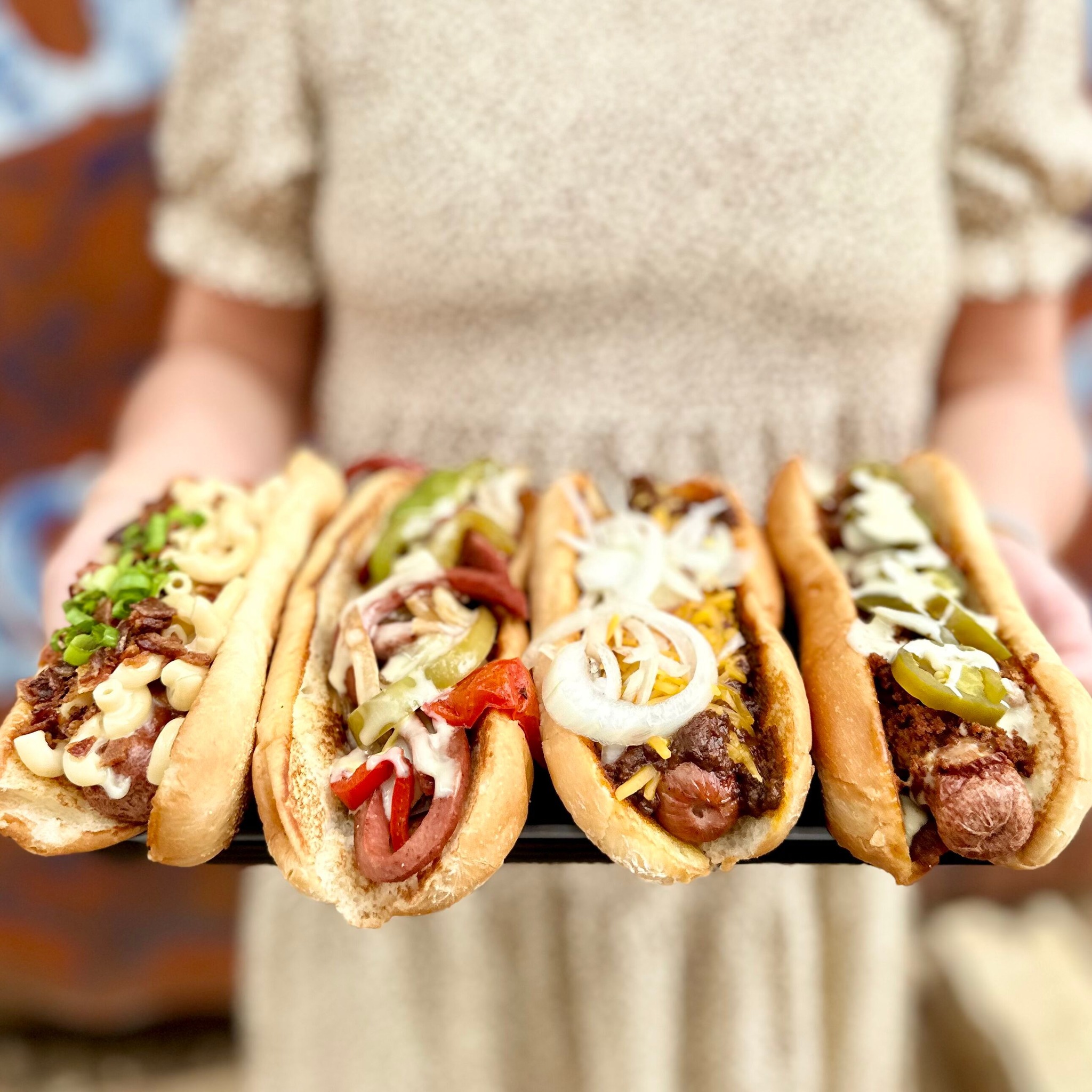 Person holding four hot dogs, each with different toppings.